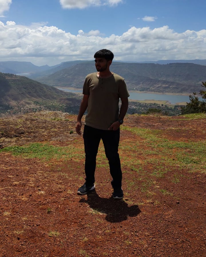 Rakshit Vyas standing on a hilltop above a valley and a lake